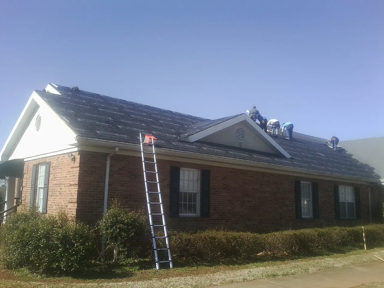 Crew tearing shingles off a brick ranch roof with a ladder set — Emergency Roof Repair work by our crew in Millbury