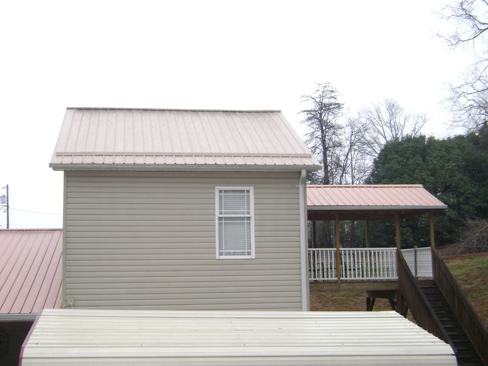 Tan metal roofs on a two story addition and attached porch, from a Roof Replacement job in Millbury